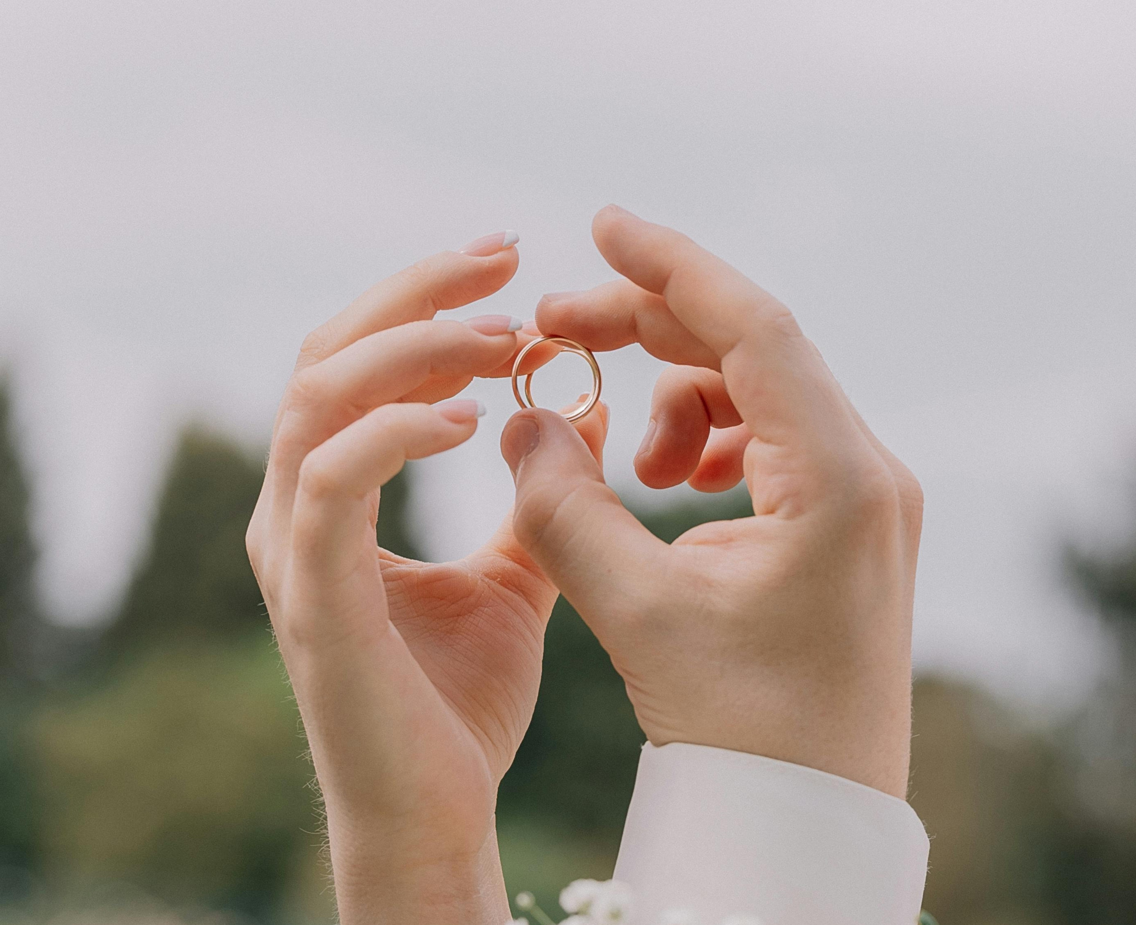 Hands forming heart around wedding rings with white flowers